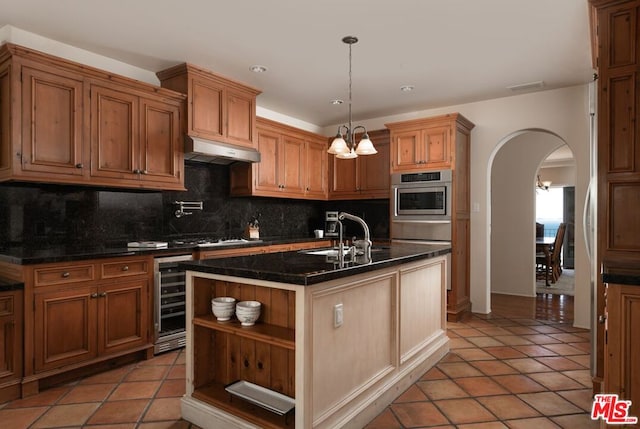 kitchen with wine cooler, a kitchen island with sink, light tile patterned flooring, and decorative light fixtures