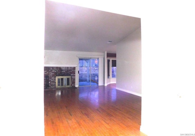 unfurnished living room with wood-type flooring and a brick fireplace