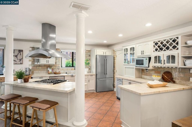 kitchen with ornate columns, white cabinets, island exhaust hood, kitchen peninsula, and stainless steel appliances