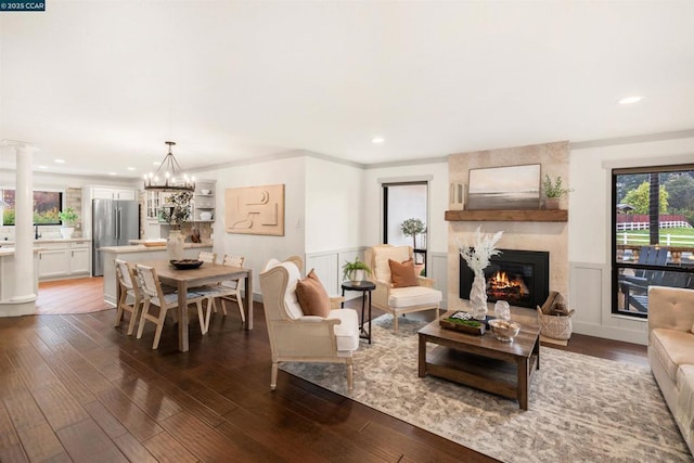 living room featuring decorative columns, crown molding, a large fireplace, and dark hardwood / wood-style flooring