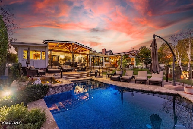 pool at dusk featuring an in ground hot tub, a patio, and an outdoor hangout area