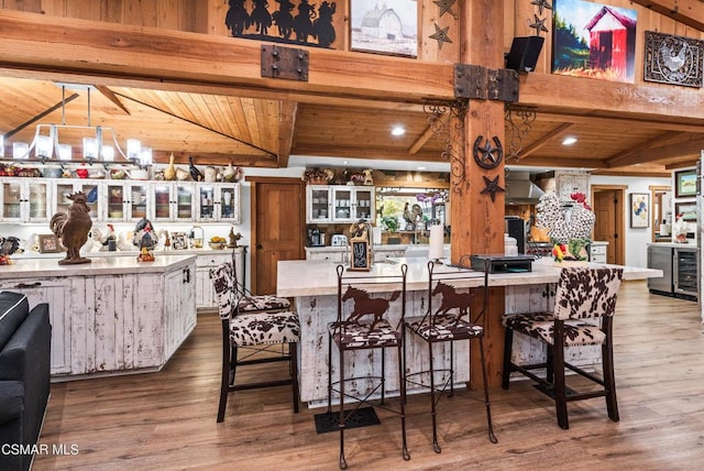 kitchen with a kitchen bar, wall chimney exhaust hood, lofted ceiling with beams, wooden ceiling, and hardwood / wood-style floors