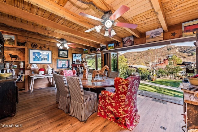 dining area featuring wooden walls, beamed ceiling, a mountain view, and wood-type flooring