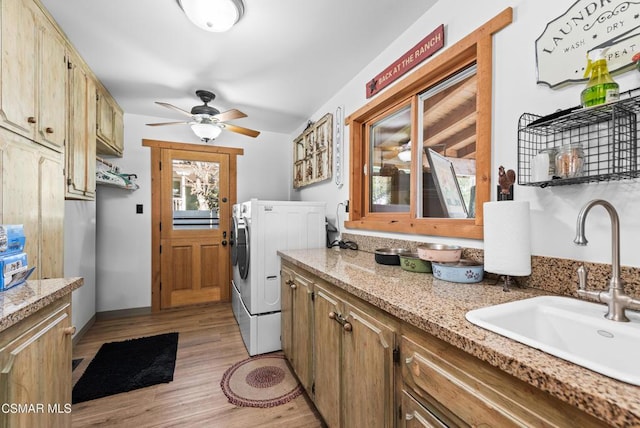 clothes washing area featuring washing machine and dryer, ceiling fan, sink, and light wood-type flooring