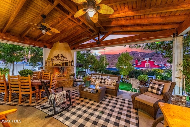 patio terrace at dusk featuring an outdoor living space with a fireplace, ceiling fan, and a gazebo