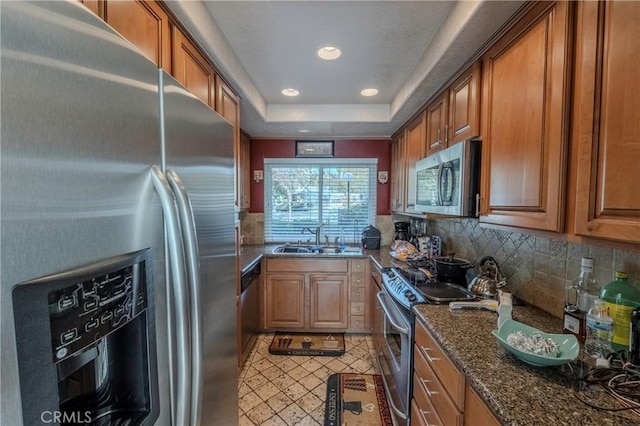 kitchen with sink, stainless steel appliances, tasteful backsplash, dark stone counters, and a tray ceiling