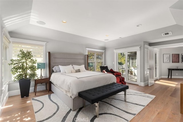 bedroom with light hardwood / wood-style flooring, access to outside, and a raised ceiling