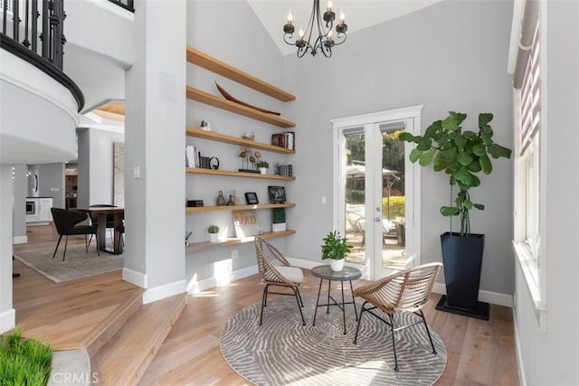 sitting room featuring light wood-type flooring, a chandelier, high vaulted ceiling, and french doors