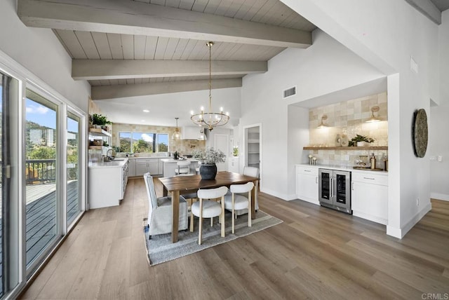 dining area with light wood-type flooring, wine cooler, vaulted ceiling with beams, and an inviting chandelier