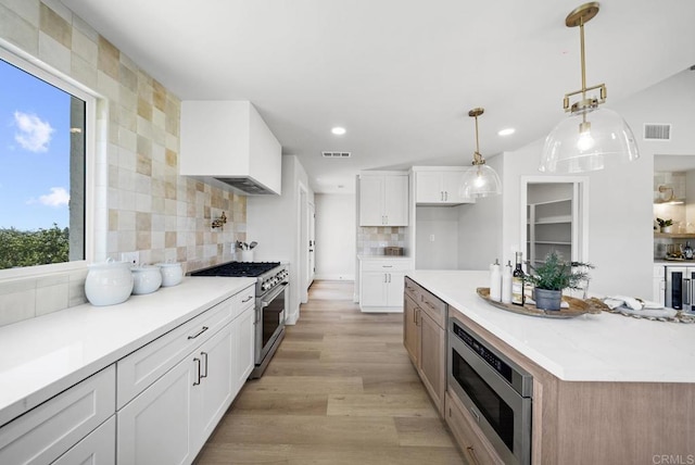 kitchen with white cabinetry, a healthy amount of sunlight, backsplash, hanging light fixtures, and appliances with stainless steel finishes