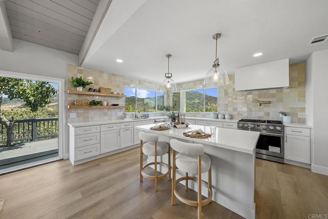 kitchen featuring light wood-type flooring, high end stove, white cabinets, decorative light fixtures, and backsplash