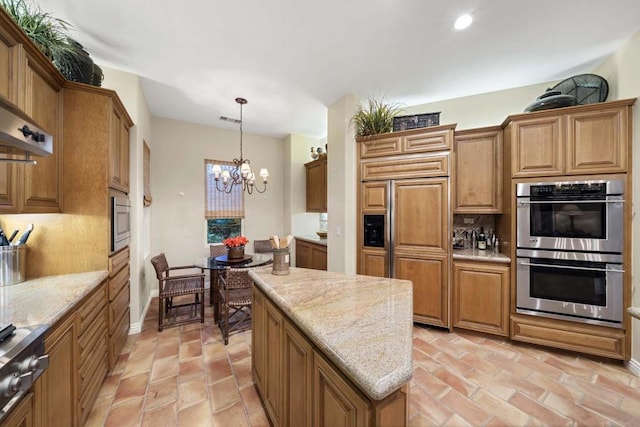 kitchen with light stone countertops, a center island, built in appliances, pendant lighting, and a chandelier