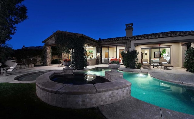 pool at night featuring an in ground hot tub and a patio