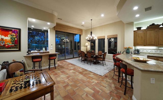 kitchen with a breakfast bar area, crown molding, pendant lighting, and a notable chandelier