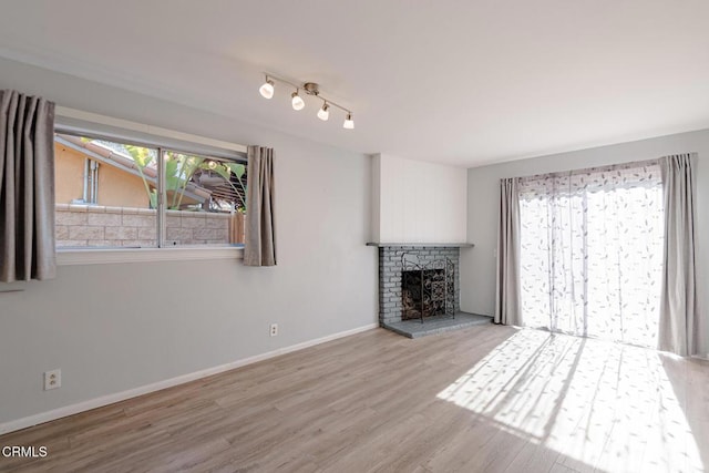 unfurnished living room featuring light wood-type flooring, track lighting, and a brick fireplace