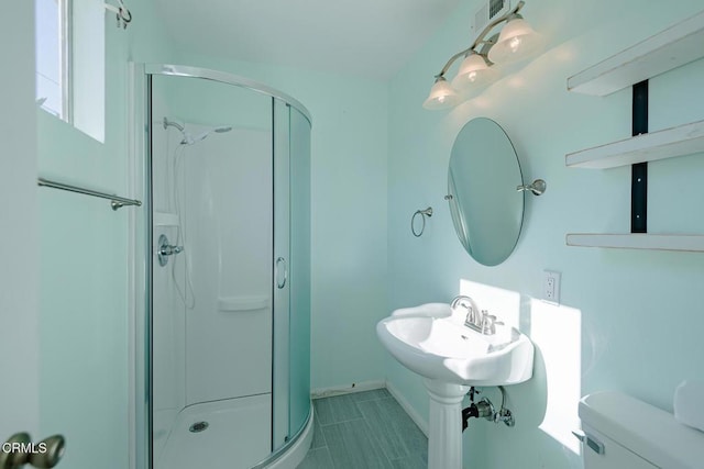 bathroom featuring toilet, a shower with door, and sink