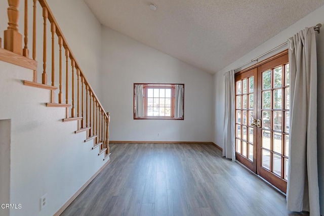 empty room with a textured ceiling, vaulted ceiling, dark wood-type flooring, and french doors