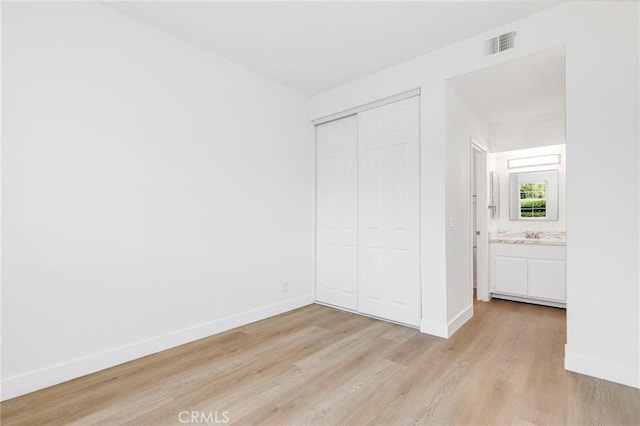 unfurnished bedroom featuring light hardwood / wood-style floors, ensuite bathroom, and a closet