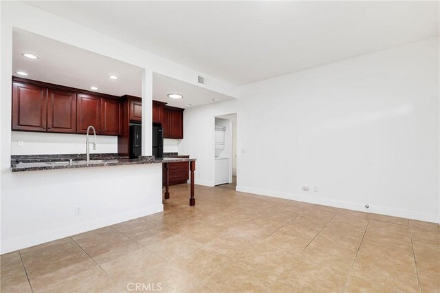 kitchen with sink, black fridge, dark stone countertops, light tile patterned floors, and kitchen peninsula