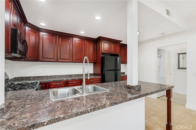 kitchen with dark stone countertops, black appliances, kitchen peninsula, sink, and light tile patterned flooring