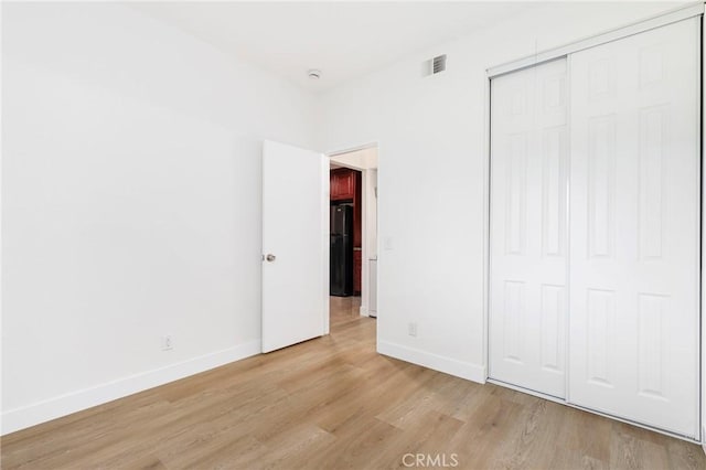 unfurnished bedroom featuring black fridge, light wood-type flooring, and a closet