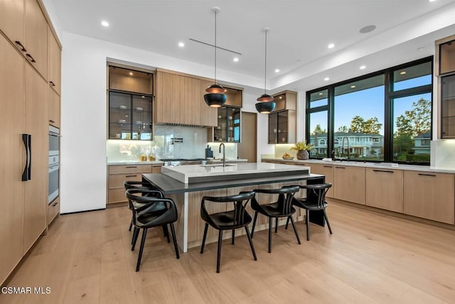 kitchen with a kitchen island with sink, light brown cabinets, light hardwood / wood-style floors, and decorative light fixtures