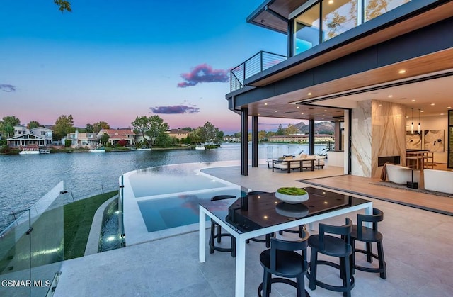 patio terrace at dusk featuring a balcony, a water view, and exterior bar