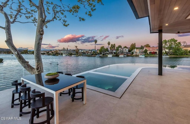 pool at dusk with a patio area, an in ground hot tub, and a water view