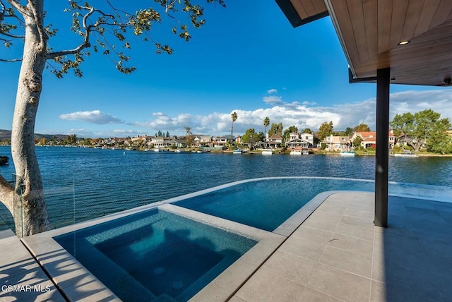 exterior space with an in ground hot tub, a patio, and a water view