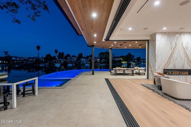 pool at night featuring a water view and a premium fireplace