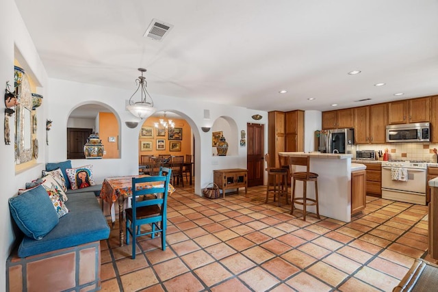 kitchen featuring decorative backsplash, appliances with stainless steel finishes, a kitchen breakfast bar, light tile patterned floors, and hanging light fixtures