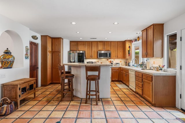 kitchen with light tile patterned flooring, sink, a kitchen island, a kitchen bar, and stainless steel appliances