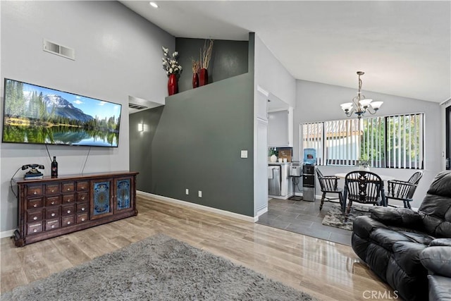 living room with a notable chandelier, light hardwood / wood-style floors, and vaulted ceiling