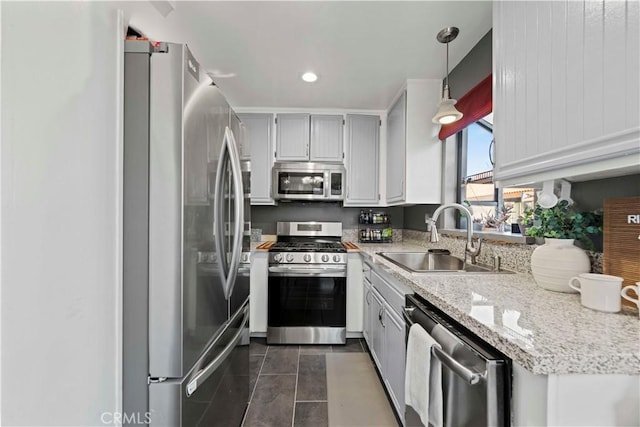 kitchen with light stone countertops, hanging light fixtures, stainless steel appliances, dark tile patterned flooring, and sink