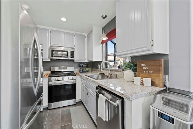 kitchen with light stone countertops, decorative light fixtures, white cabinets, appliances with stainless steel finishes, and sink