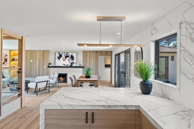 kitchen with a fireplace, light stone counters, light wood-type flooring, and hanging light fixtures