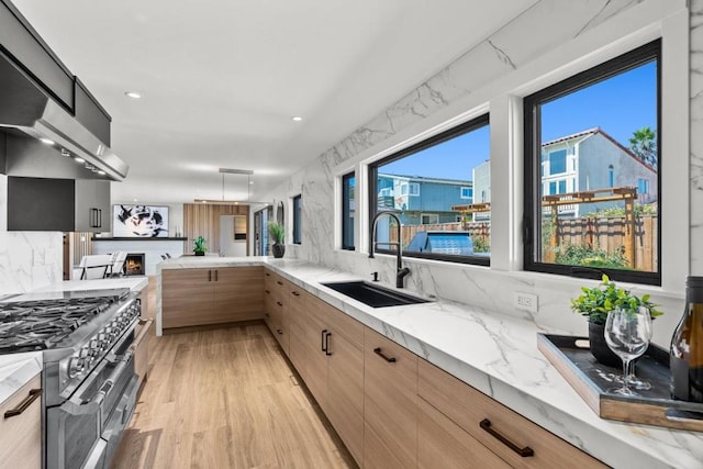 kitchen with light stone countertops, sink, light brown cabinets, light hardwood / wood-style flooring, and double oven range