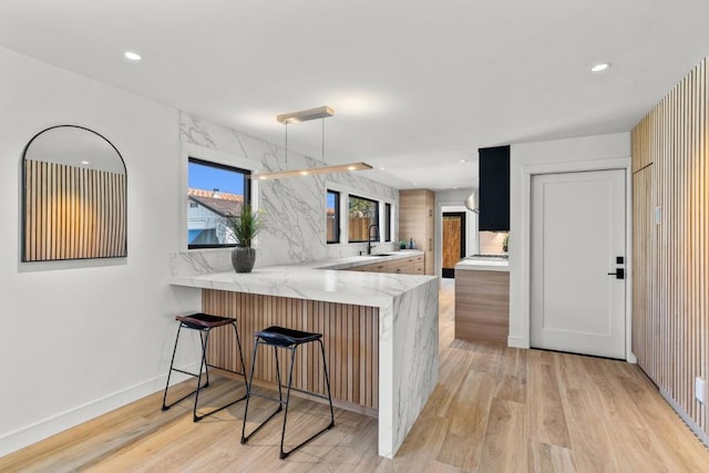 kitchen featuring kitchen peninsula, a kitchen breakfast bar, light stone countertops, sink, and light hardwood / wood-style flooring