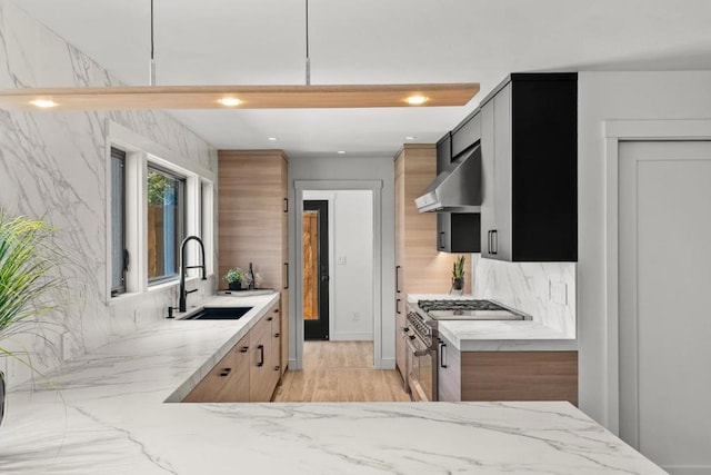 kitchen with sink, wall chimney range hood, tasteful backsplash, light stone counters, and double oven range