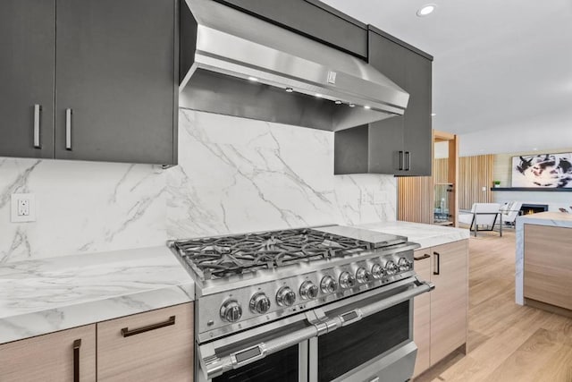 kitchen featuring decorative backsplash, light stone counters, wall chimney exhaust hood, double oven range, and light hardwood / wood-style floors