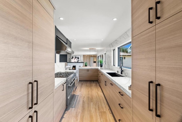 kitchen featuring sink, stainless steel range, tasteful backsplash, light stone counters, and kitchen peninsula