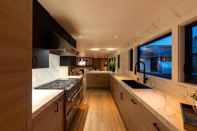 kitchen with double oven range, backsplash, sink, light stone countertops, and range hood