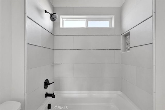 bathroom with tiled shower / bath combo and toilet