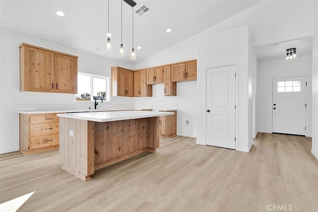 kitchen featuring sink, pendant lighting, lofted ceiling, a kitchen island, and light wood-type flooring