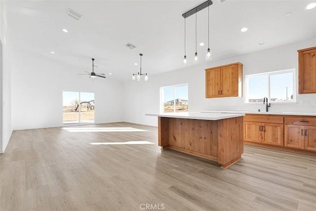 kitchen featuring light wood-type flooring, ceiling fan with notable chandelier, sink, pendant lighting, and a kitchen island