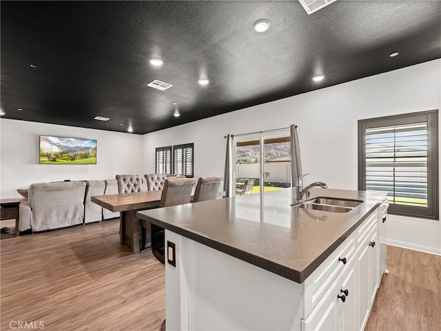 kitchen with sink, white cabinets, a kitchen island with sink, a textured ceiling, and light hardwood / wood-style flooring