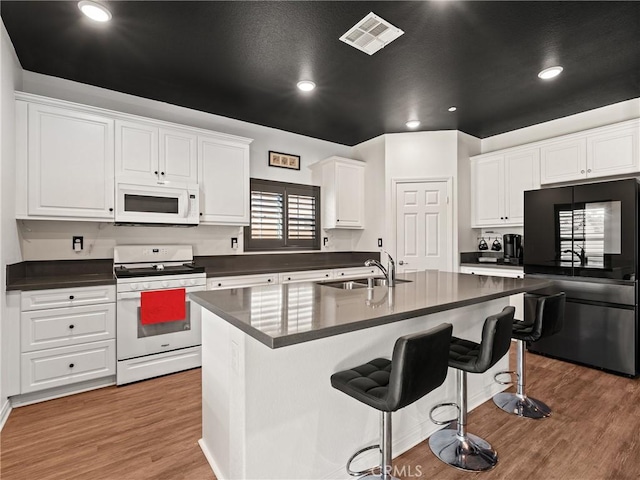 kitchen with sink, wood-type flooring, a center island with sink, white appliances, and white cabinets