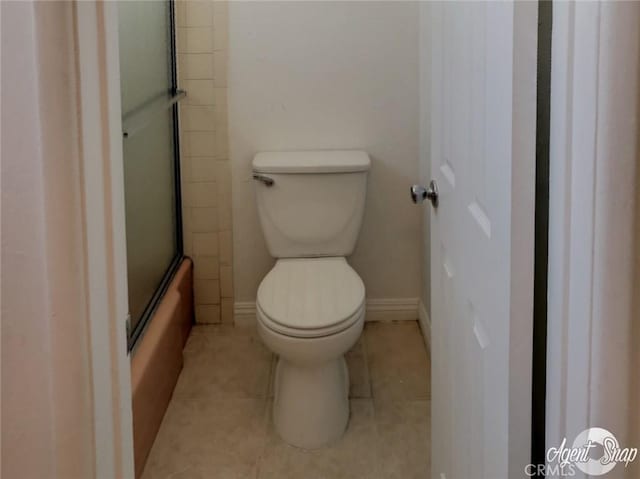 bathroom with tile patterned floors, bath / shower combo with glass door, and toilet