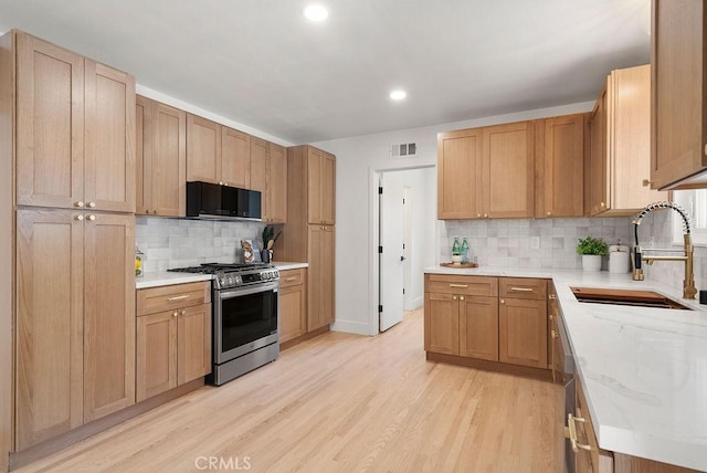 kitchen featuring tasteful backsplash, light stone counters, gas range, sink, and light hardwood / wood-style flooring