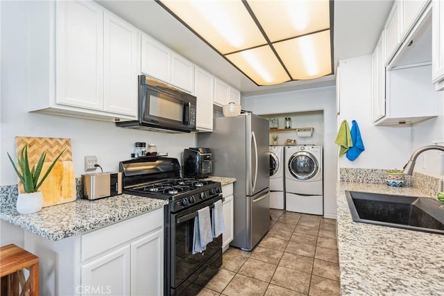 kitchen featuring black appliances, sink, independent washer and dryer, light stone counters, and white cabinetry